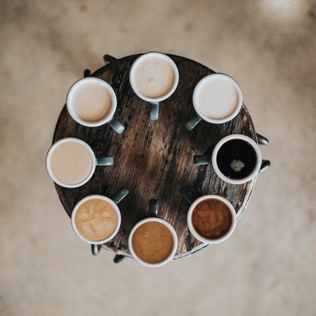 Neun Kaffeetassen im Kreis auf einem runden Holztisch, von oben fotografiert